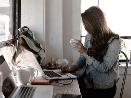 Vrouw met kop koffie aan bureau, achter beeldscherm